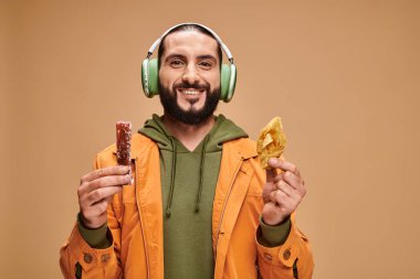 happy arabic man in headphones holding two middle eastern desserts, honey baklava and churchkhela clipart