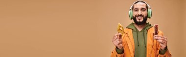 happy man in headphones holding two middle eastern desserts, honey baklava and churchkhela banner clipart
