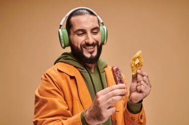 happy man in headphones holding two middle eastern desserts, honey baklava and churchkhela clipart