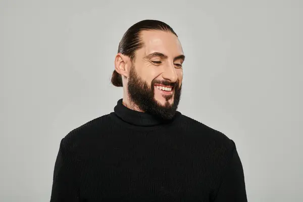 stock image portrait of good looking arabic man with beard posing in turtleneck and smiling on grey backdrop