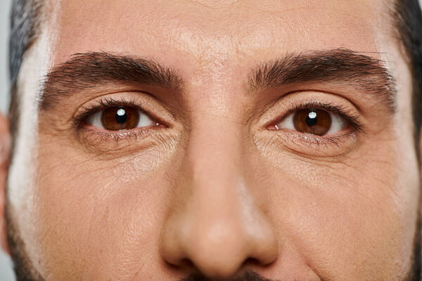 close up shot of brown eyed arabic man looking at camera g on grey background, part of face