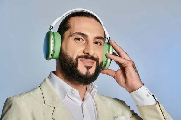 happy bearded man in elegant formal wear listening music in wireless headphones on grey background