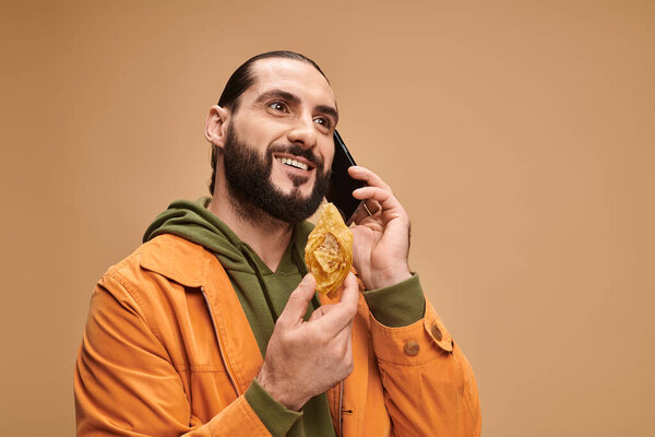 happy man holding traditional middle eastern dessert and talking on smartphone on beige, baklava