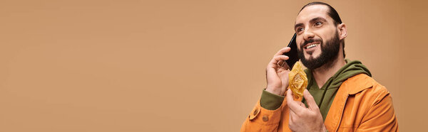 happy man holding middle eastern dessert and talking on smartphone on beige, baklava banner