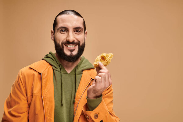 happy man holding honey baklava and looking at camera on beige, traditional middle eastern dessert