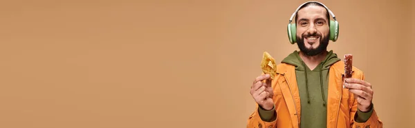 stock image happy man in headphones holding two middle eastern desserts, honey baklava and churchkhela banner