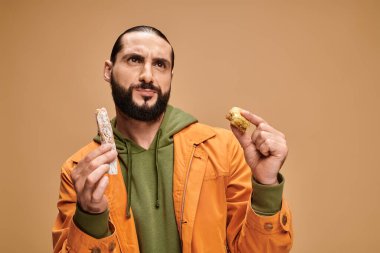 Kafası karışmış sakallı adam elinde baklava ve cevizli sucuk bej arka planda, Türk lezzetleri