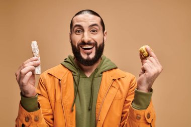 excited arabic bearded man holding baklava and cevizli sucuk on beige backdrop, turkish delights clipart