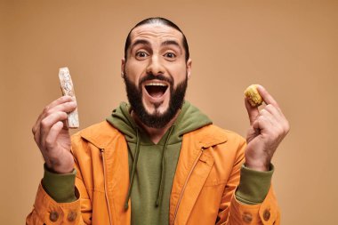 Heyecanlı Arap sakallı adam bej arka planda baklava ve cevizli sakızı tutuyor.