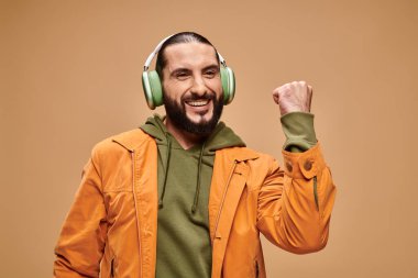Sakallı neşeli orta doğulu adam bej arka planda kablosuz kulaklıkla müzik dinliyor.