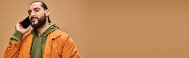 Sakallı yakışıklı orta doğulu adam bej arka planda akıllı telefondan konuşuyor.