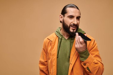 Mutlu Orta Doğulu sakallı adam bej arka planda sesli mesaj gönderiyor, akıllı telefon.