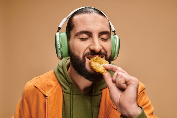 cheerful man in headphones eating delicious honey baklava on beige backdrop, turkish delights