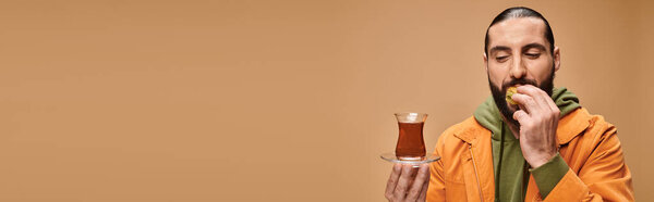 знамя счастливого бородатого мужчины, держащего турецкий чай в традиционной стеклянной чашке и поедающего вкусную пахлаву