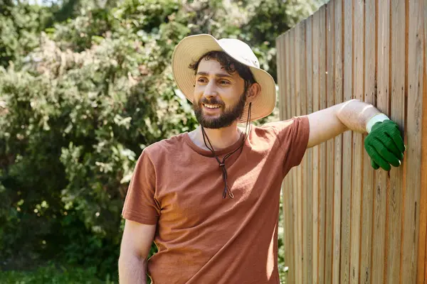 stock image handsome and bearded farmer in sun hat standing near fence in countryside, rural lifestyle