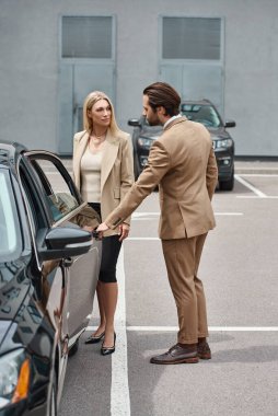 cropped view of man in formal wear opening rear door of luxury car near elegant businesswoman clipart