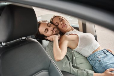 passionate and stylish couple embracing with closed eyes on drivers seat in modern car, love affair clipart