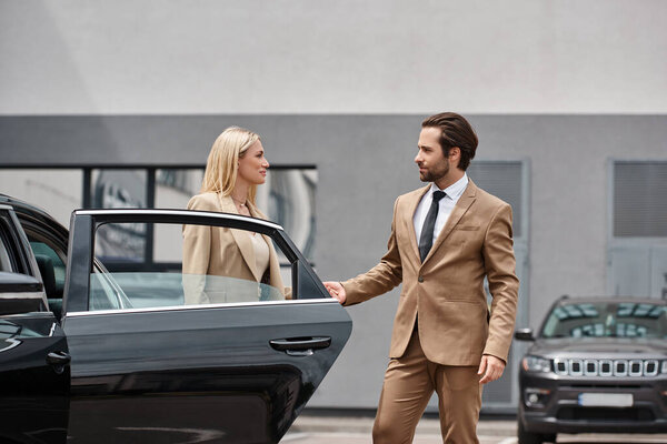 bearded elegant man and stylish blonde businesswoman holding hands near luxury car on city street