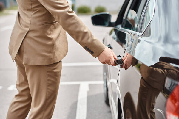 cropped view of elegant businessman in beige suit closing rear door of luxury car on urban street