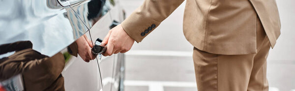 cropped view of stylish businessman in beige suit closing rear door of luxury car street, banner
