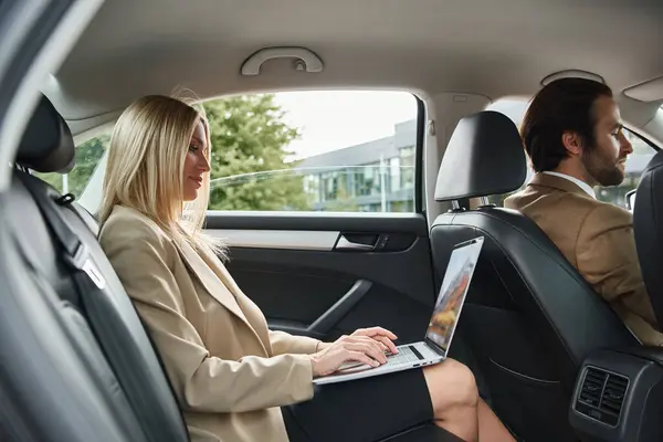 stock image blonde elegant businesswoman typing on laptop near elegant man driving luxury car on street