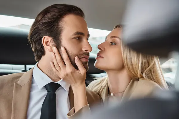 alluring blonde businesswoman touching face of handsome colleague in car, seduction and love affair
