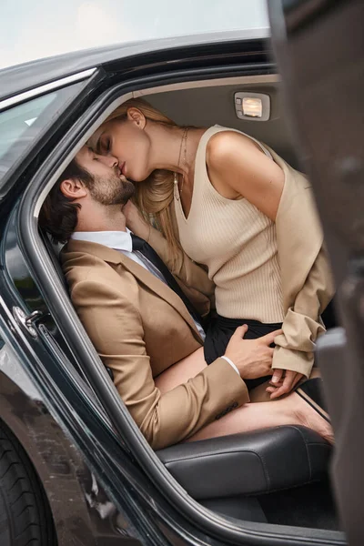 successful business couple  in elegant formal wear embracing and kissing in luxury car, love affair