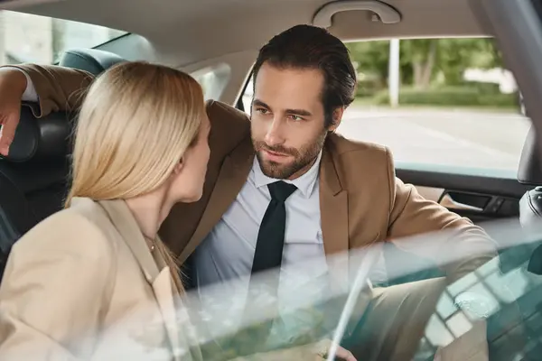 attractive businessman looking at blonde female colleague and seducing her during travel in car