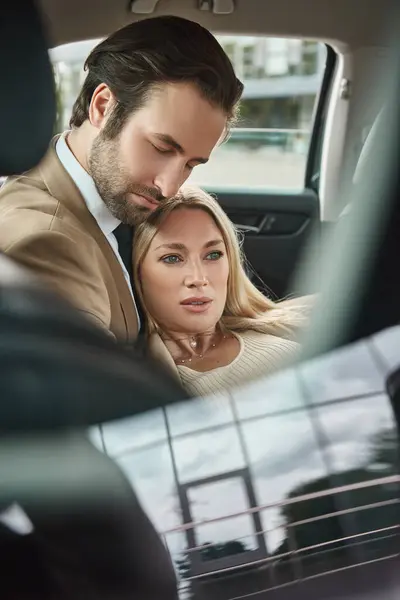elegant businessman with closed eyes hugging sensual blonde woman in luxury car, love affair