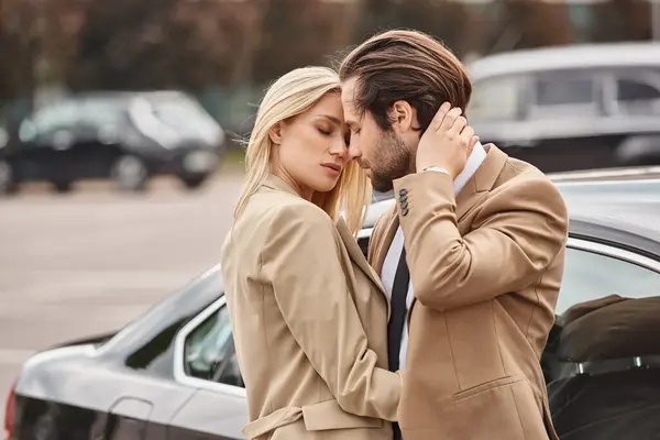 successful business couple in elegant formal wear embracing near car on urban street, love affair