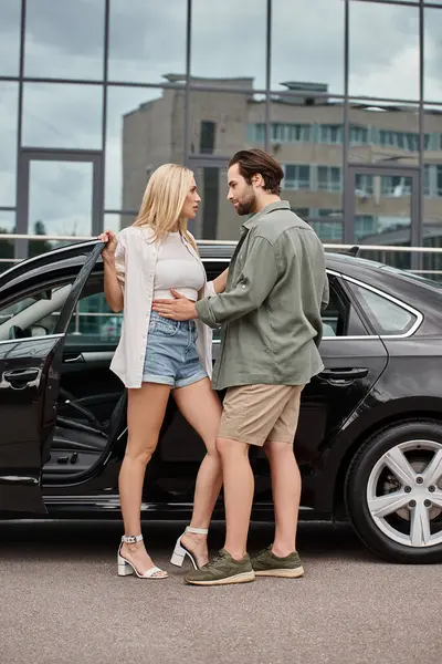 attractive blonde woman and stylish bearded man in stylish casual clothes embracing near car