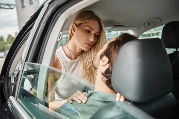attractive blonde woman seducing man sitting in modern car on urban street, romantic love dating