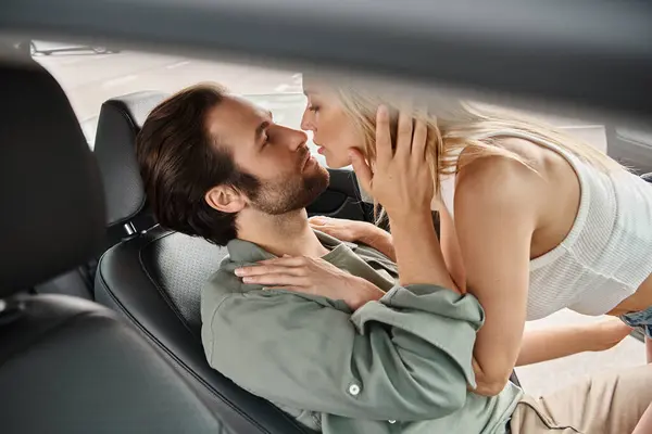passionate blonde woman seducing handsome bearded man on drivers seat in modern car, urban romance