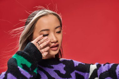 young asian woman with dyed hair in sweater with animal print posing with hand near face, wind clipart