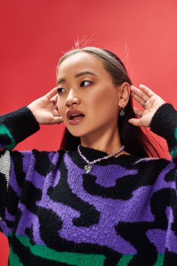 Canlı süveter giymiş, kırmızı arka fona bakan güzel Asyalı manken.