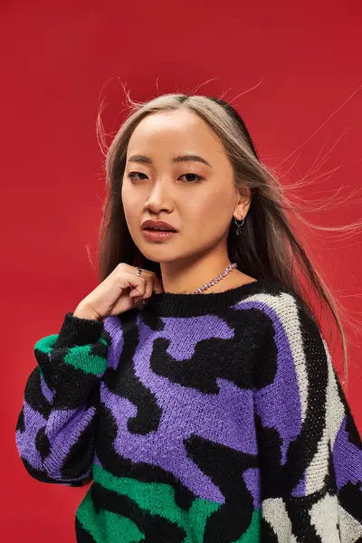 stock image beautiful young asian woman with dyed hair in vibrant sweater with animal print posing on red