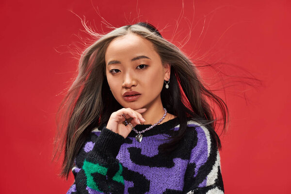 wind blowing at face of attractive young asian woman with dyed hair in sweater with animal print