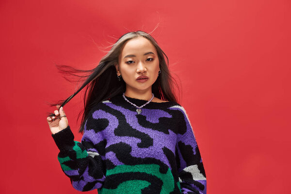 красивая молодая азиатка в ярком свитере с отпечатком животного с ожерельем в форме сердца на красном