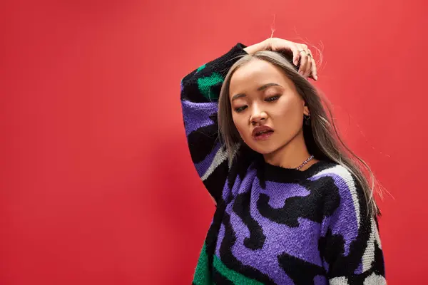 stock image pretty young asian woman in sweater with animal print with heart shaped necklace posing on red