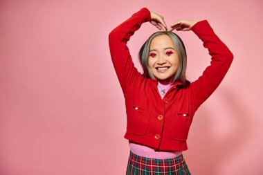 Sevgililer Günü konsepti, kırmızı ceketli mutlu Asyalı kadın elleri pembe arka planda olan kalbi gösteriyor.
