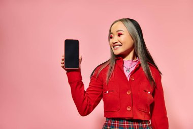 Kırmızı sevgililer günü makyajlı mutlu Asyalı kadın pembe ekranlı akıllı telefon gösteriyor.