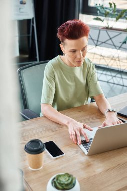 Modern ofise gitmek için akıllı telefon ve kahvenin yanındaki dizüstü bilgisayarda çalışan hırslı, hırslı bir ibne.