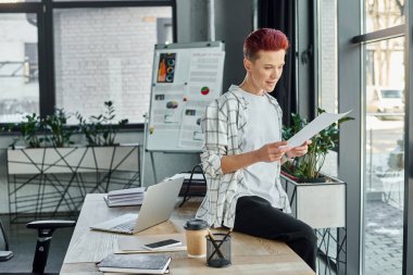 non-binary person working with documents while sitting on work desk near devices and coffee to go clipart