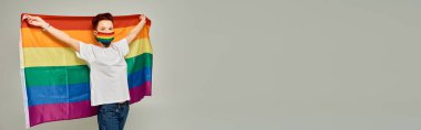 Gökkuşağı renginde kızıl saçlı tuhaf bir model. Gri, yatay pankartta LGBT bayrağı taşıyor.