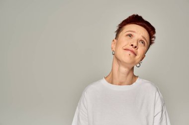 Düşünceli ve rüya gibi kızıl saçlı beyaz tişörtlü çift cinsiyetli manken gri renkli duyguları görmezden geliyor.