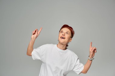 Beyaz tişörtlü, çift cinsiyetli birinin yukarı bakıp parmaklarıyla gri hayrete düşmesine şaşırdım.