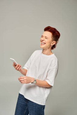 Beyaz tişörtlü, akıllı telefonlu, gri gözleriyle gülen aşırı neşeli kızıl saçlı ibne.