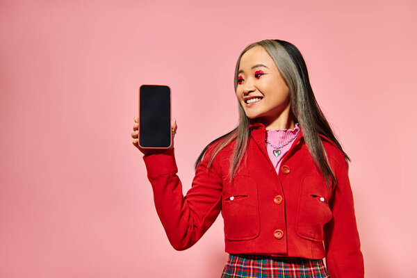 happy asian woman with red Valentines day makeup showing smartphone with blank screen on pink