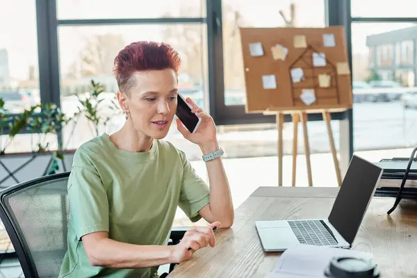 non-binary business person talking on mobile phone near laptop with blank screen in modern office