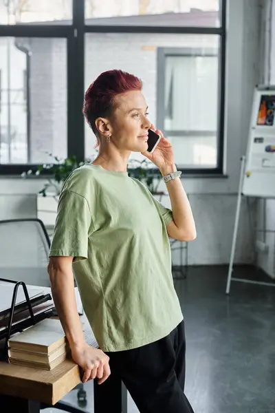 stylish non-binary manager in casual attire talking on smartphone while standing in modern office